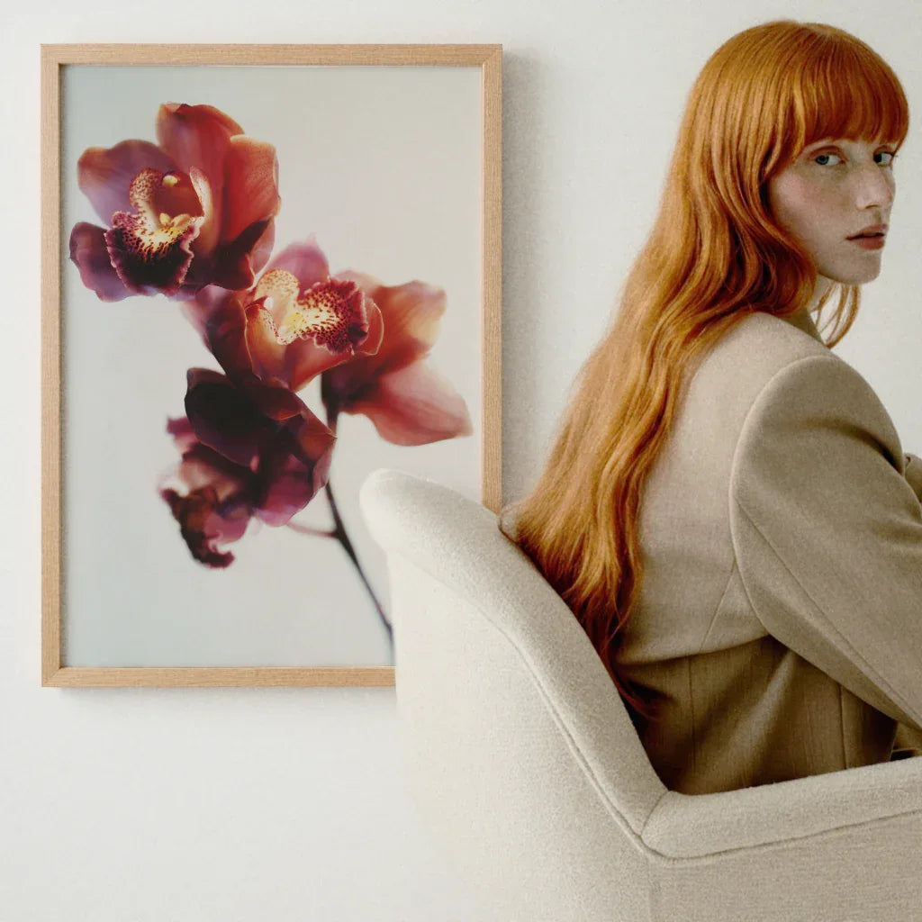 Orchideen Poster im Holzrahmen vor einer Person mit langen roten Haaren in beiger Kleidung